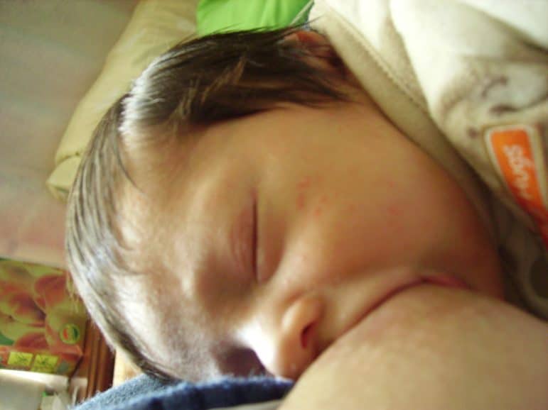 Close up photo of a young baby latched on nursing, with their eyes closed